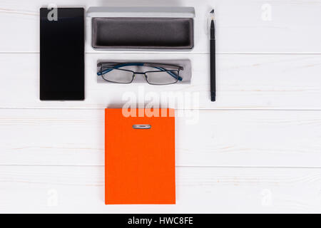 Orange-Tagebuch mit einem Stift für die Organisation eines Zeitplans, stilvolle Gläser und offenen Fall für Gläser in der Nähe von Handy auf weißer Holztisch Stockfoto