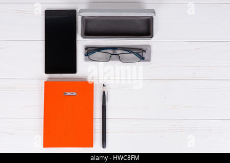 Orange-Tagebuch mit einem Stift für die Organisation eines Zeitplans, Gläser und offenen Fall für Gläser in der Nähe von Handy auf weißer Holztisch Stockfoto