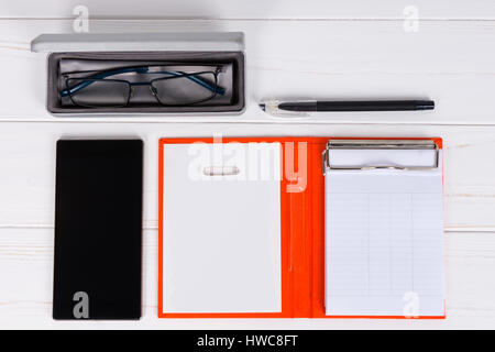 Nahaufnahme von Tagebuch mit einem Stift, stilvolle Gläser in offenen Fall für Gläser in der Nähe von Handy auf weißer Holztisch Stockfoto
