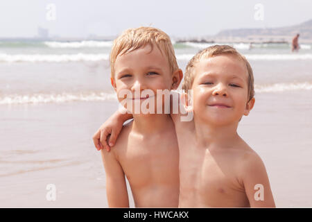 Zwei niedliche entzückenden kleinen Brüder jungen sitzen auf dem Strand Meer