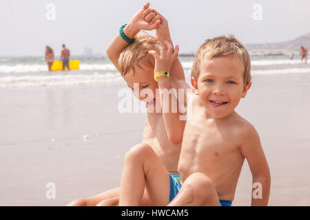 Zwei niedliche entzückenden kleinen Brüder jungen sitzen auf dem Strand Meer