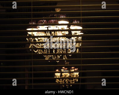 Zwei alte Kronleuchter aus Glas mit Kristall weißen Licht, eine scharf, einen weiteren streut darüber hinaus hinter modernen horizontalen Louvre blind beleuchtet Stockfoto