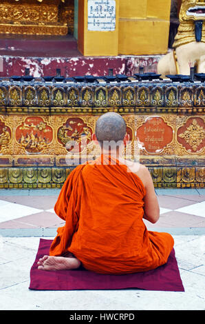 Ein junger Mönch sitzt auf einer Matte vor der Shwedagon-Pagode, Yangon, Myanmar Stockfoto