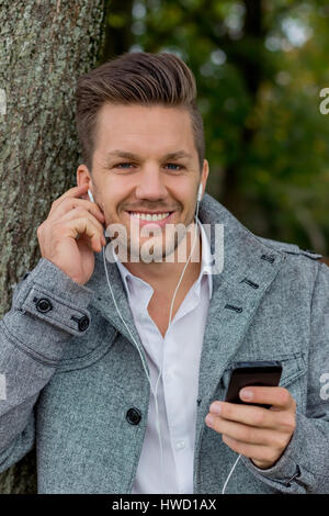 Ein Mann hört Musik mit dem Handy. Unterhaltung auf dem Handy, Ein Mann Hört Musik Mit handlichen Dachmarke. Partnervertrag bin Mobiltelefon. Stockfoto
