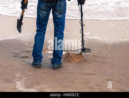 Mann mit einem Metall-Detektor für Metall oder verlorenen Schatz am Sandstrand suchen. Er hat Showel in der hand Stockfoto