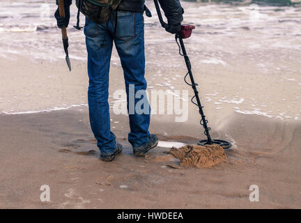 Mann mit einem Metall-Detektor für Metall oder verlorenen Schatz am Sandstrand suchen. Er hat Showel in der hand Stockfoto