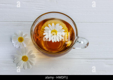 Tasse Kamillentee mit Kamillenblüten auf einem Holztisch Stockfoto