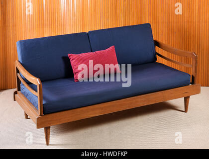High Angle Stillleben View of Vintage Holz Sofa mit Navy blauen und roten Kissen im Wohnzimmer mit beigen Teppich und Holz Wandverkleidung Stockfoto