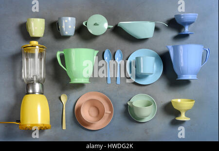 Auswahl an bunten Retro-Kunststoff Geschirr mit einem Mixer, Teller, Tassen und Krüge in ordentlichen Reihen auf einem grauen Hintergrund von oben gesehen Stockfoto