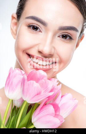 Schöne lächelnde Frau mit rosa Tulpen in der Nähe von Gesicht auf weiß Stockfoto