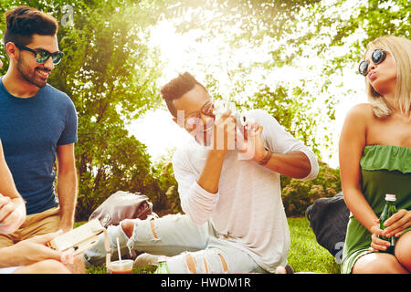 Erwachsene Freunde fotografieren mit Sofortbild-Kamera beim Picknick im park Stockfoto