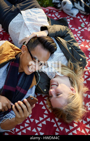 Draufsicht eines Paares auf der Picknickdecke Kopfhörer Musik austauschen Stockfoto