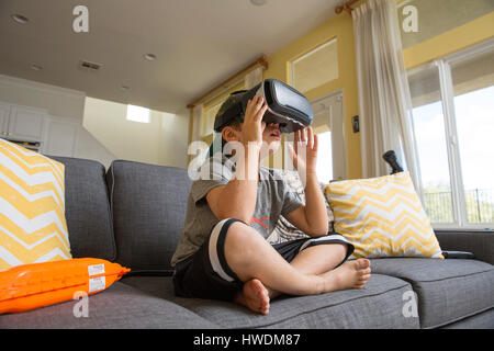 Kleiner Junge Schneidersitz auf Sofa sitzen, tragen von virtual-Reality-Kopfhörer Stockfoto