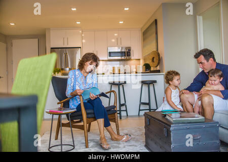 Vater und zwei kleine Kinder sitzen auf Sofa, Großmutter sitzt im Stuhl, Blick durch Magazin Stockfoto