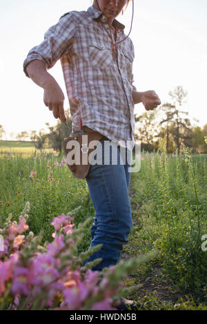 Frau, die Schere aus Werkzeuggürtel im Löwenmaul (Antirrhinum) Blume Bauernhof Feld entfernen Stockfoto