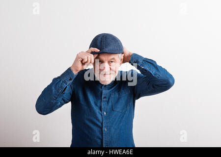 Senior woman in Jeanshemd und flache Kappe lächelnd, Studioaufnahme. Stockfoto