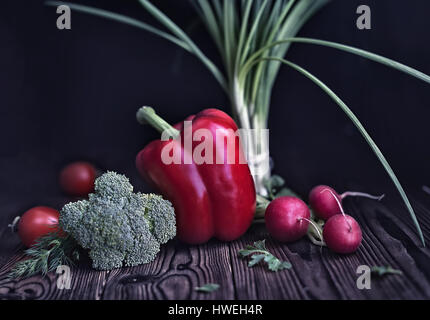 Stillleben mit roter Paprika, Radieschen, Tomaten, Frühlingszwiebeln und Kohl auf alten rustikalen Holztisch Hintergrund, dunkel getönten, Stil, Konzept vegetarisches Essen, c Stockfoto
