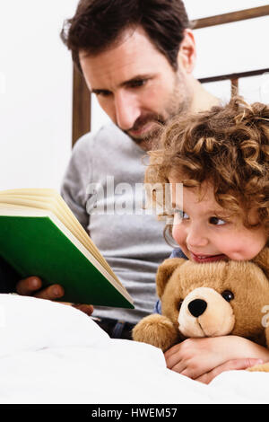 Mädchen, Teddy Bären umarmen, während Vater Märchenbuch im Bett liest Stockfoto