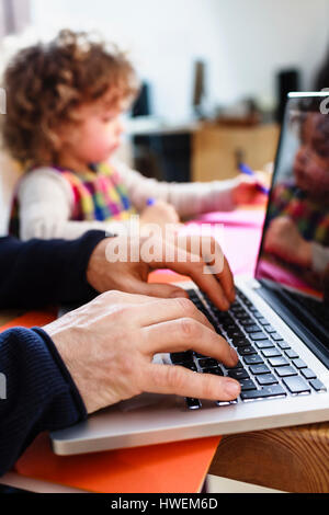 Nahaufnahme eines Mannes Hände Tippen auf Laptop und Tochter Zeichnung am Tisch Stockfoto