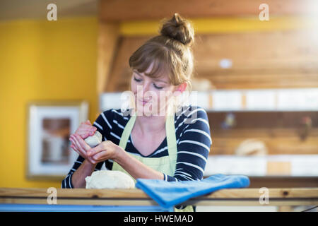 Junge Frau arbeitet in der Bäckerei, Rollen Teig in Händen Stockfoto