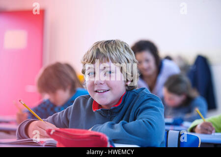 Porträt eines jungen im Klassenzimmer sitzen am Schreibtisch, Lächeln Stockfoto