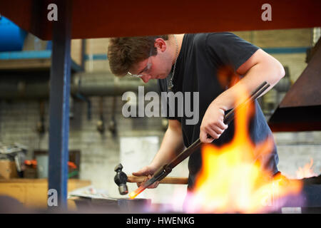 Junge männliche Auszubildende Schmied Hämmern rote Roheisen auf Workshop-Amboss Stockfoto