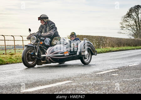 Ältere Mann und Enkel fahren Motorrad und Beiwagen entlang Landstraße Stockfoto