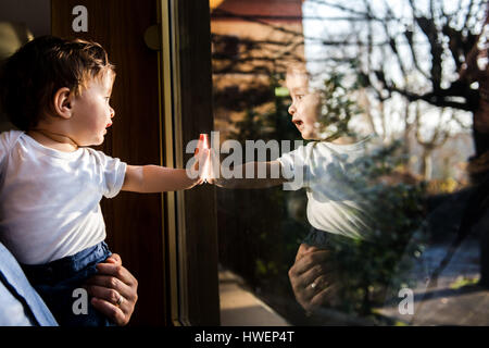 Baby Junge in den Armen des Vaters auf der Suche durch und berührende Fenster Stockfoto