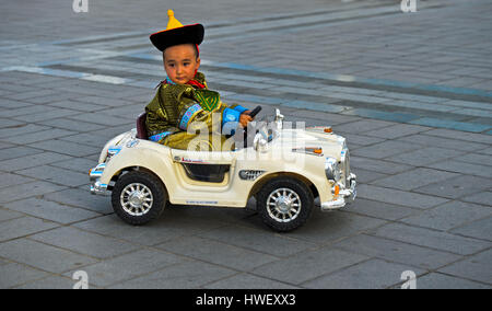 Junge in eine traditionelle Deel Kostüme fahren eine elektrische Spielzeugauto, mongolischen National Kostüm Festival, Ulaanbaatar, Mongolei Stockfoto