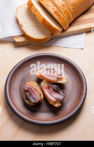 Nahaufnahme der leckere gebackene Kartoffeln mit Scheiben Speck in braun Ton Platte auf Holz- Hintergrund. Scheiben geräucherter Speck auf Kartoffeln. Stockfoto