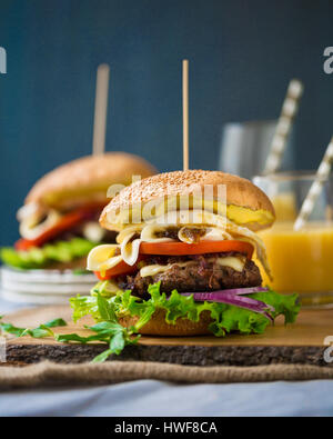 Zwei hausgemachte Burger mit frischem Gemüse, Fleisch, karamellisierten Zwiebeln und Käse auf Holzbrett Stockfoto