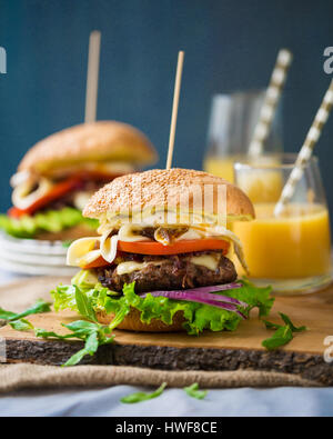 Zwei hausgemachte Burger mit frischem Gemüse, Fleisch, karamellisierten Zwiebeln und Käse auf Holzbrett Stockfoto