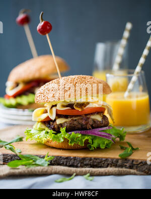 Zwei hausgemachte Burger mit frischem Gemüse, Fleisch, karamellisierten Zwiebeln und Käse auf Holzbrett Stockfoto