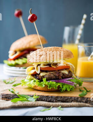 Zwei hausgemachte Burger mit frischem Gemüse, Fleisch, karamellisierten Zwiebeln und Käse auf Holzbrett Stockfoto