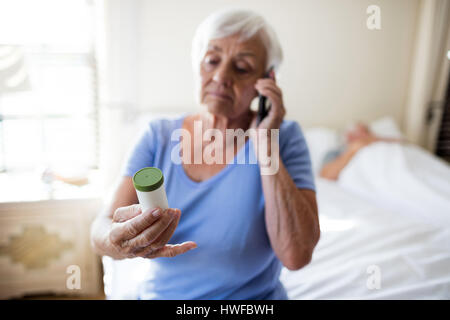 Frau am Handy sprechen und halten Medizinfläschchen Rezept im Schlafzimmer zu Hause Stockfoto