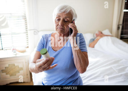 Frau am Handy sprechen und halten Medizinfläschchen Rezept im Schlafzimmer zu Hause Stockfoto