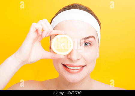 Natürliche Gesichtsmasken Konzept mit junge Frau und eine frische Zitronenscheibe auf gelbem Hintergrund Stockfoto