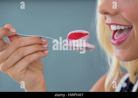 Clos-Up der schönen Frau Essen Erdbeeren mit Sahne vor grauem Hintergrund Stockfoto