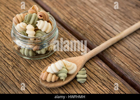 Glas und Löffel gefüllt mit Nudeln auf Holzuntergrund Stockfoto
