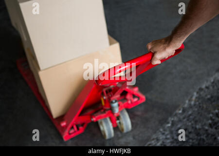 Hand des Arbeitnehmers ziehen Wagen beladen mit Kisten im Lager beschnitten Stockfoto