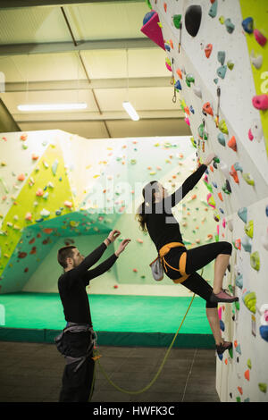 Trainer unterstützen Frau beim Klettern an künstlichen Wand im Fitness-Studio Stockfoto