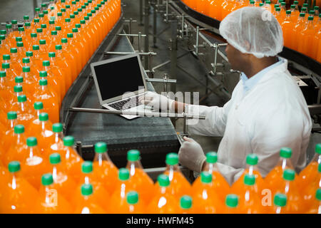 Erhöhte Ansicht der männlichen Arbeitnehmer mit Laptop inmitten Produktionslinie in Fruchtsaft Fabrik Stockfoto