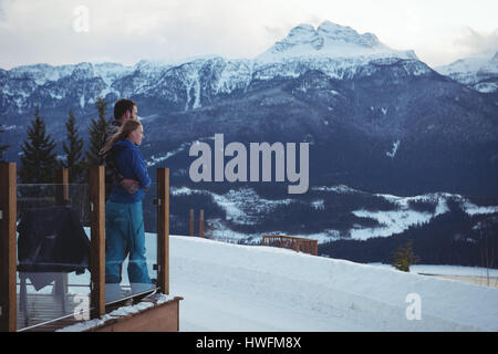 Paar im stehen durch Geländer gegen schneebedeckte Berge umarmen Stockfoto