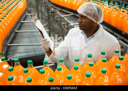 Vogelperspektive anzeigen der männlichen Arbeitnehmer Zwischenablage zu lesen, während Inspektion Flaschen Saft Fabrik Stockfoto