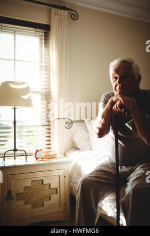 Nachdenklicher senior Mann mit seinem Gehstock im Schlafzimmer zu Hause Stockfoto