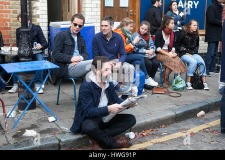 LONDON, UK - 22. April 2016: Die Menschen sitzen vor dem Café genießen Sie die Sonne. Ein Mann liest eine Zeitung, sitzend auf dem Bürgersteig. Stockfoto