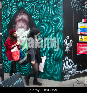 LONDON, ENGLAND - 12. Juli, 2016A Mädchen in einem roten Mantel mit einer Freundin geht von einer Mauer, Graffiti bemalt Stockfoto