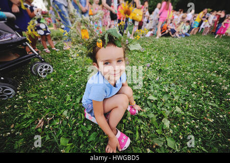 Kleines Mädchen in einen Kranz aus Blumen auf einem Hintergrund von Menschen Stockfoto