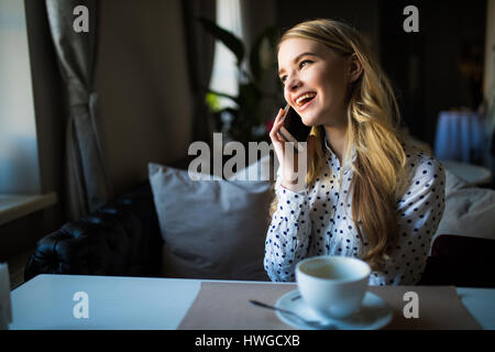 glückliche Frau im Gespräch mit Mobiltelefon beim Sitzen im Café beim Frühstück am Morgen Stockfoto