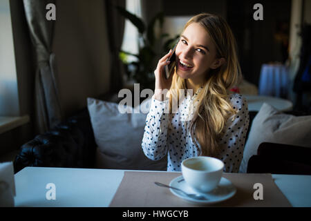 charmante Lady mit schönen Lächeln Gespräch am Mobiltelefon beim Sitzen im Café in der Mittagspause Stockfoto